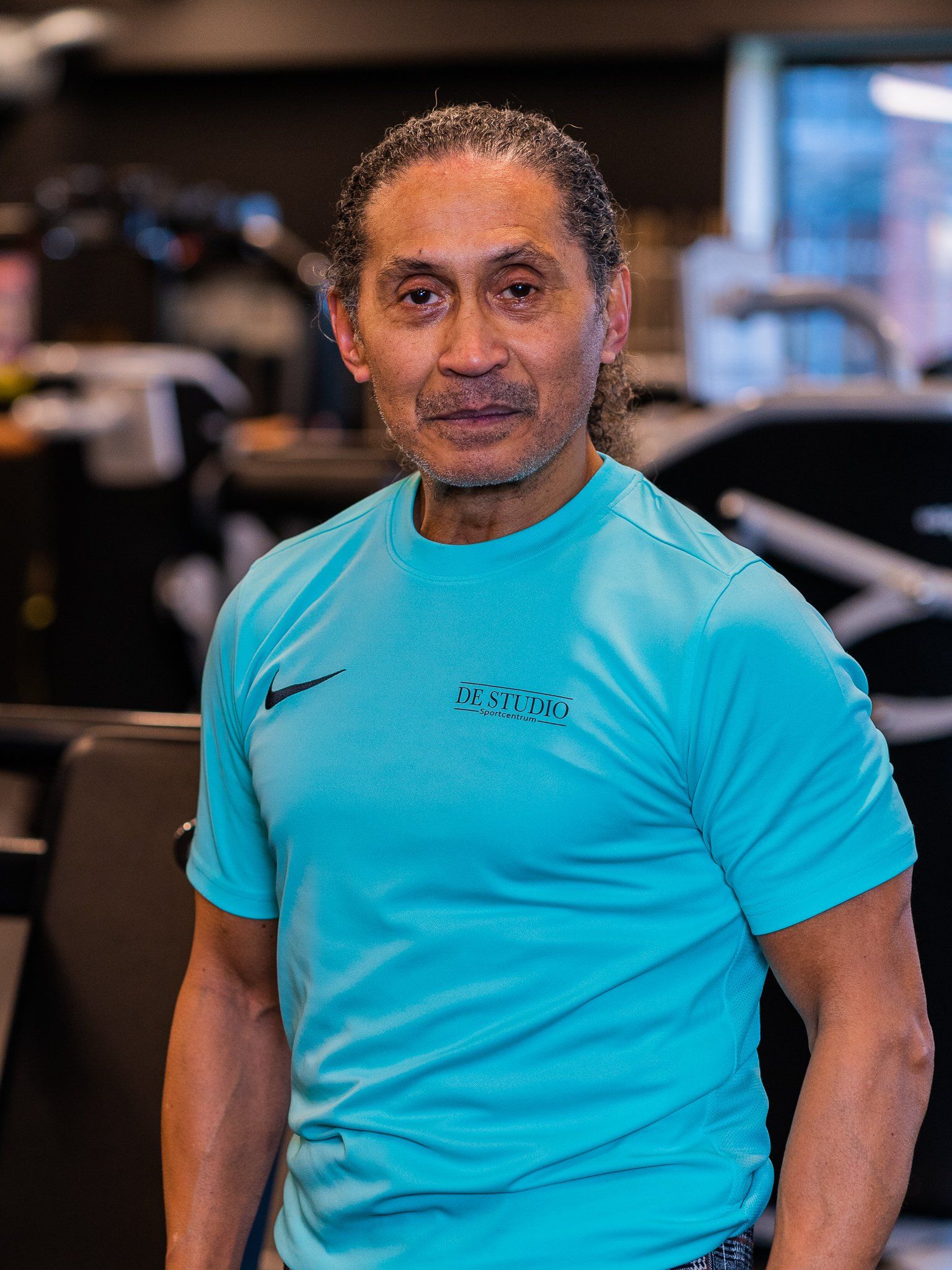 Een man in een blauw shirt staat in een sportschool.