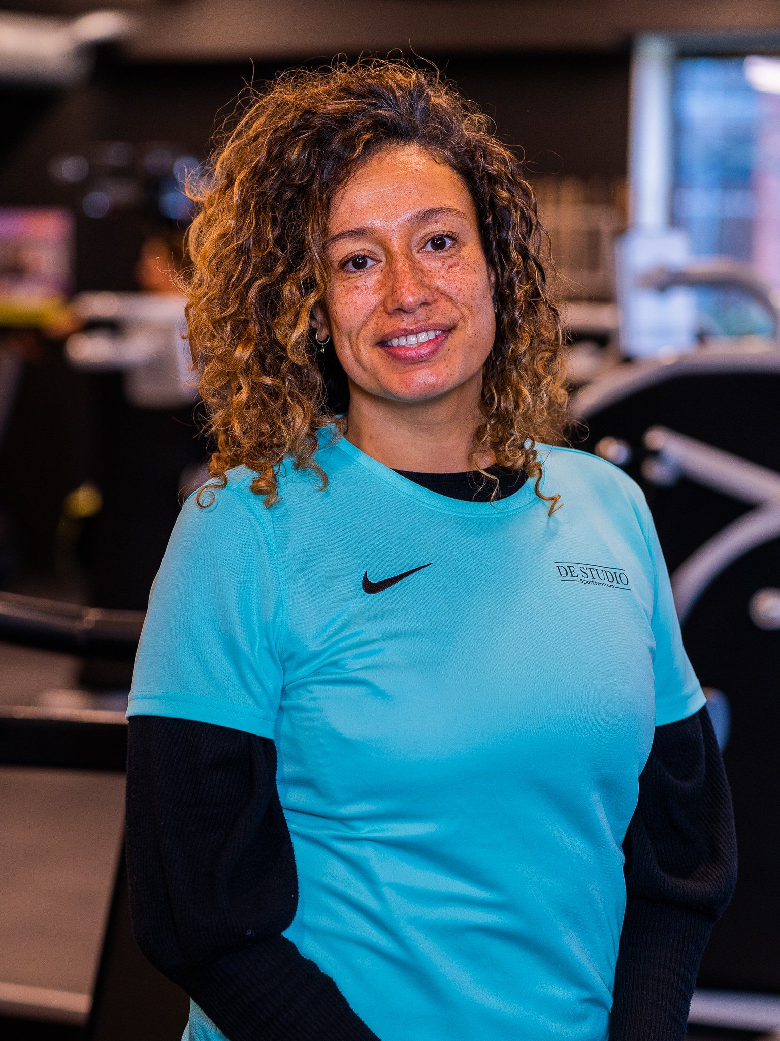 Een vrouw in een blauw Nike-shirt lacht in een sportschool.