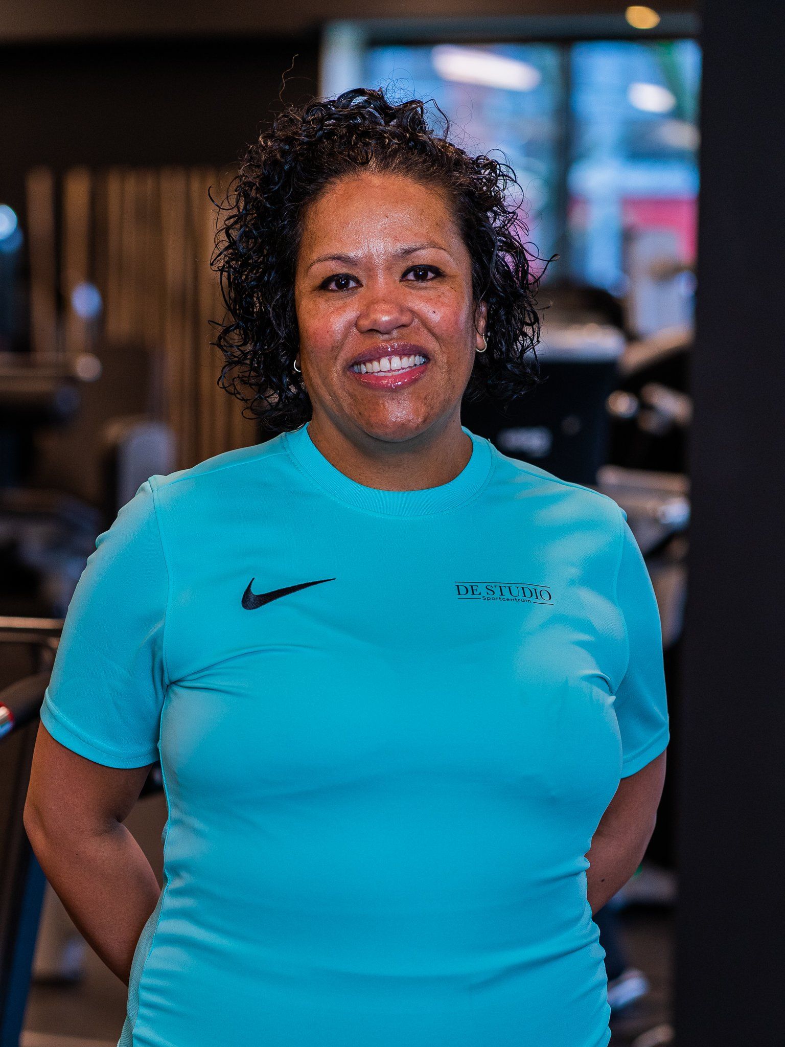 Een vrouw in een blauw Nike-shirt lacht in een sportschool.