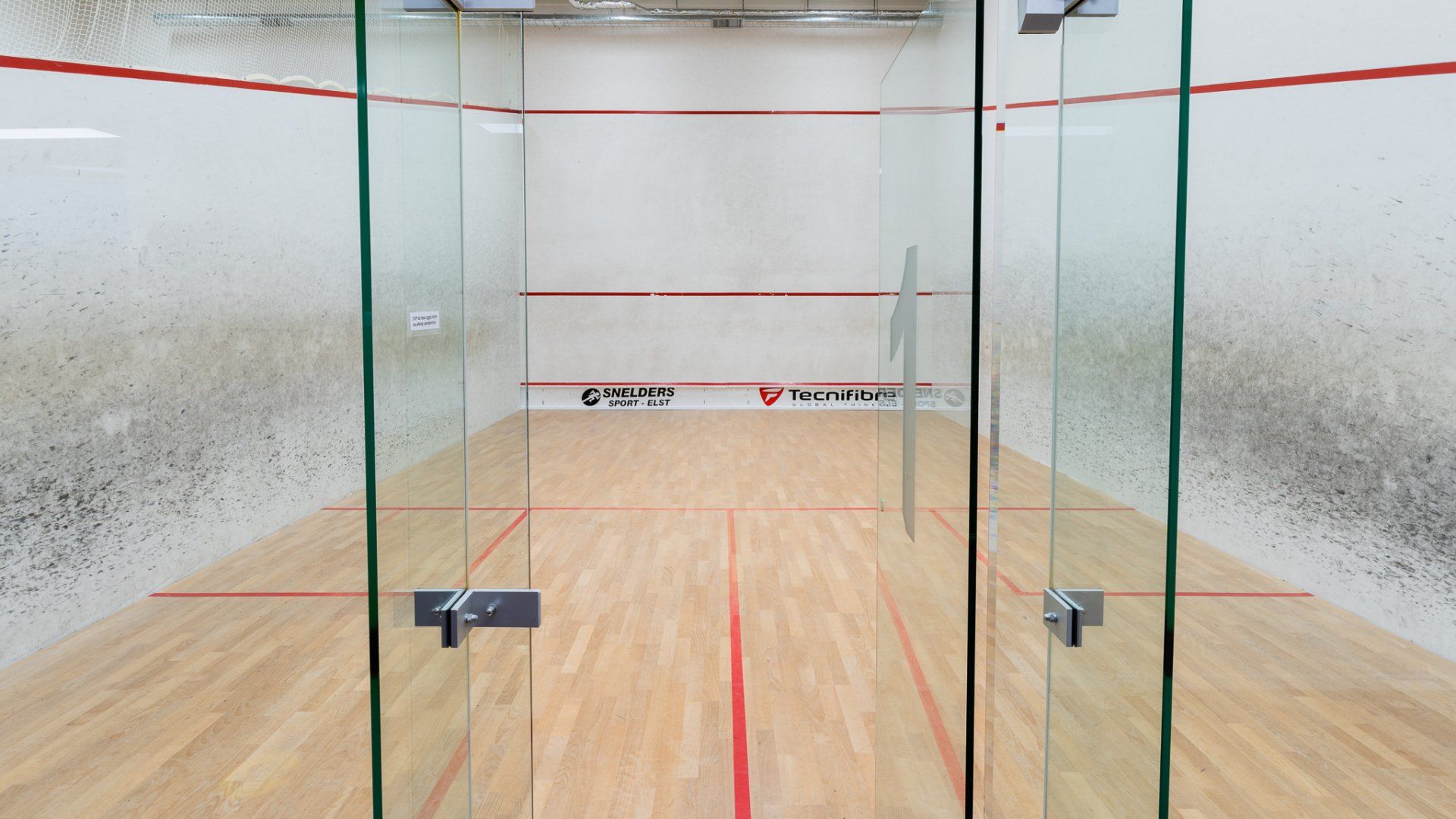 Een squashbaan met een houten vloer en glazen wanden