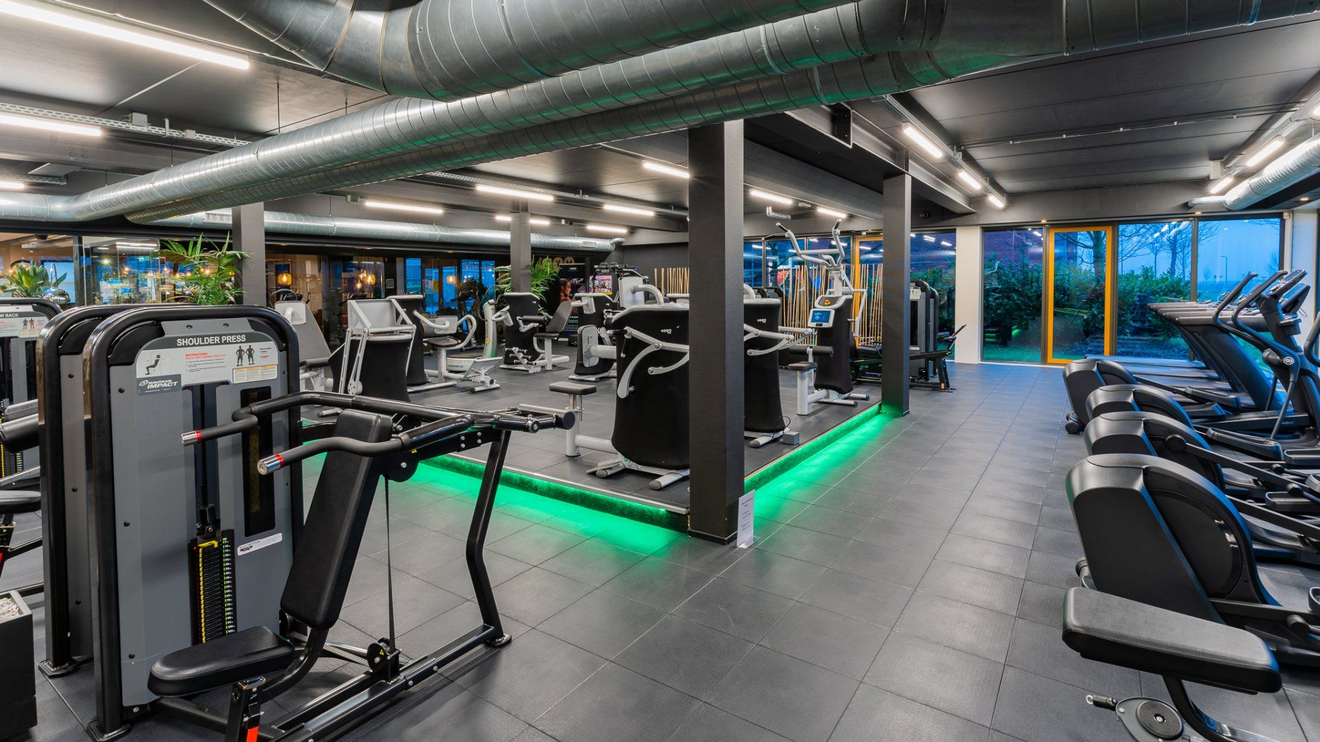 Een sportschool vol met veel fitnessapparatuur en groen licht.