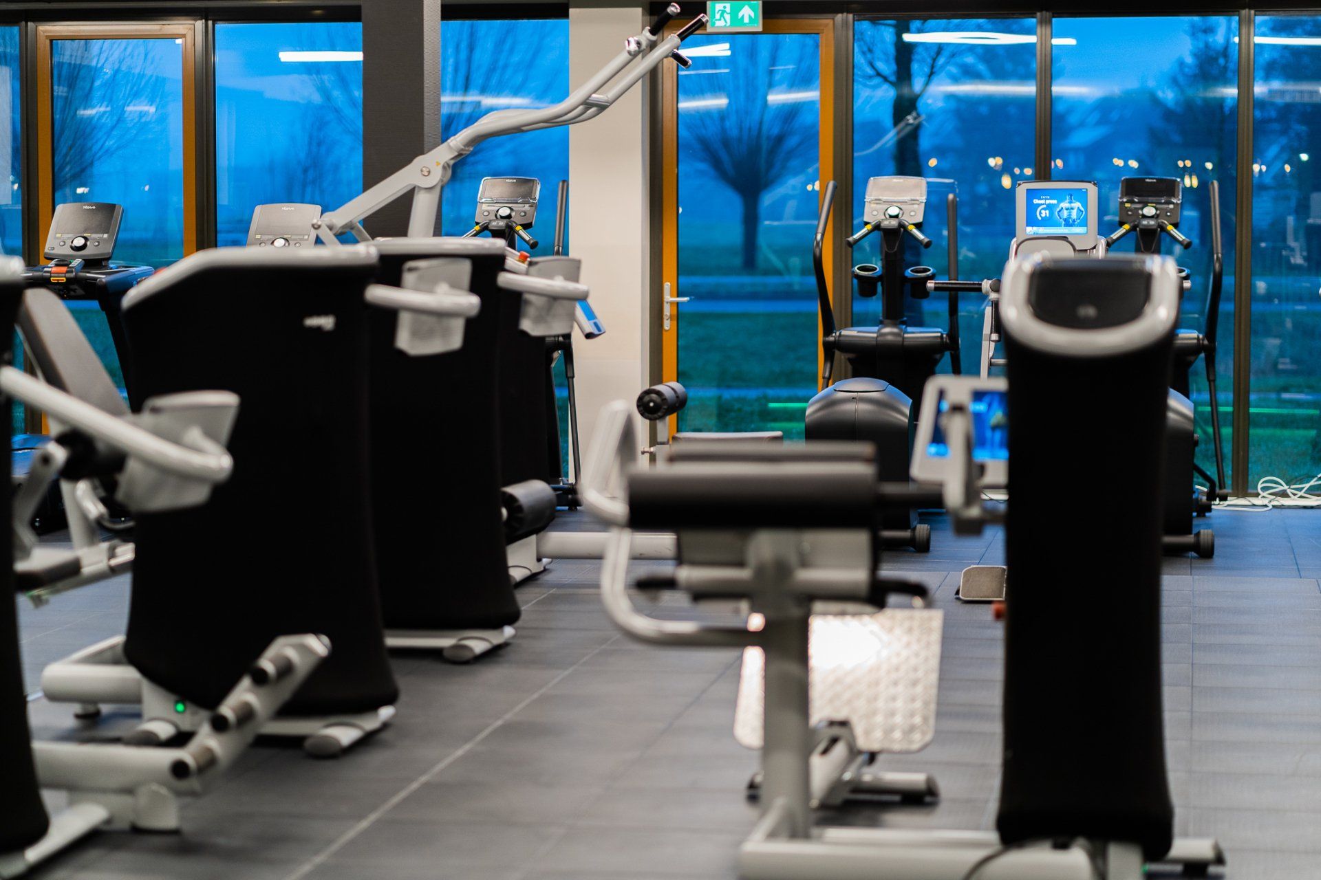 Een sportschool vol met veel fitnessapparatuur en veel ramen.