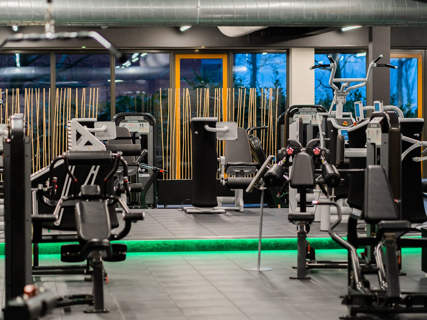 Een sportschool vol met veel fitnessapparatuur en groen licht.
