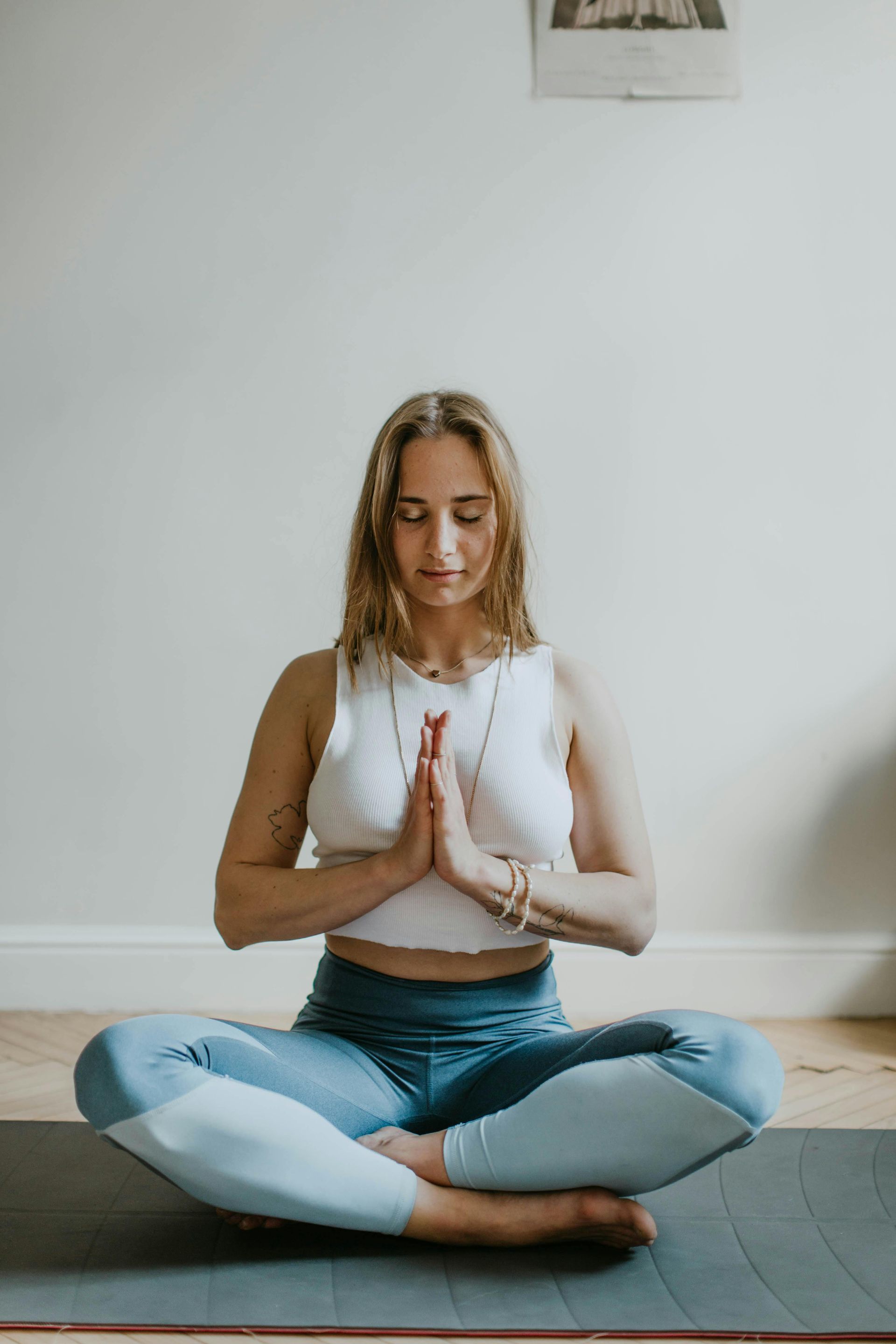 Een vrouw zit in lotushouding op een yogamat met haar ogen dicht.