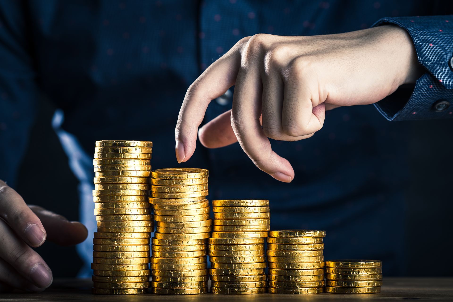 Maður er að stafla gullpeningum hver ofan á annan á borð.
