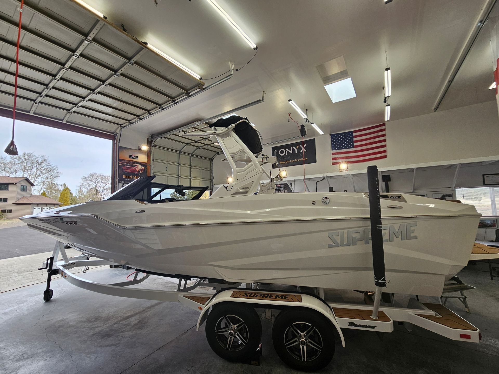 White Supreme wake boat on trailer inside a garage with an American flag.