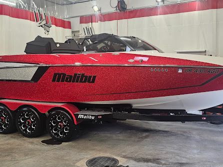 Red and white Malibu boat on a black trailer in an indoor setting.