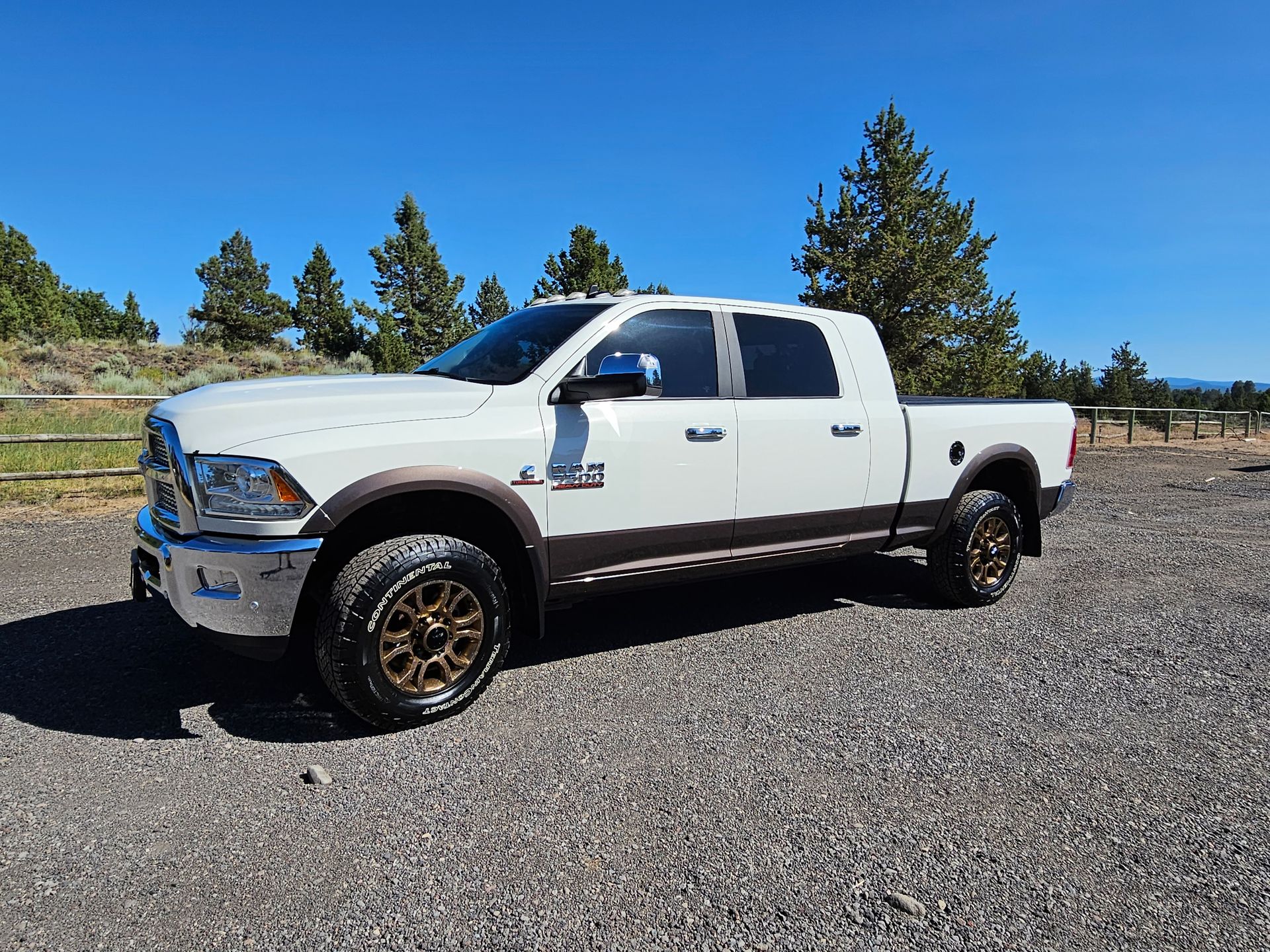 White and brown Ram pickup truck parked on gravel, sunny day.