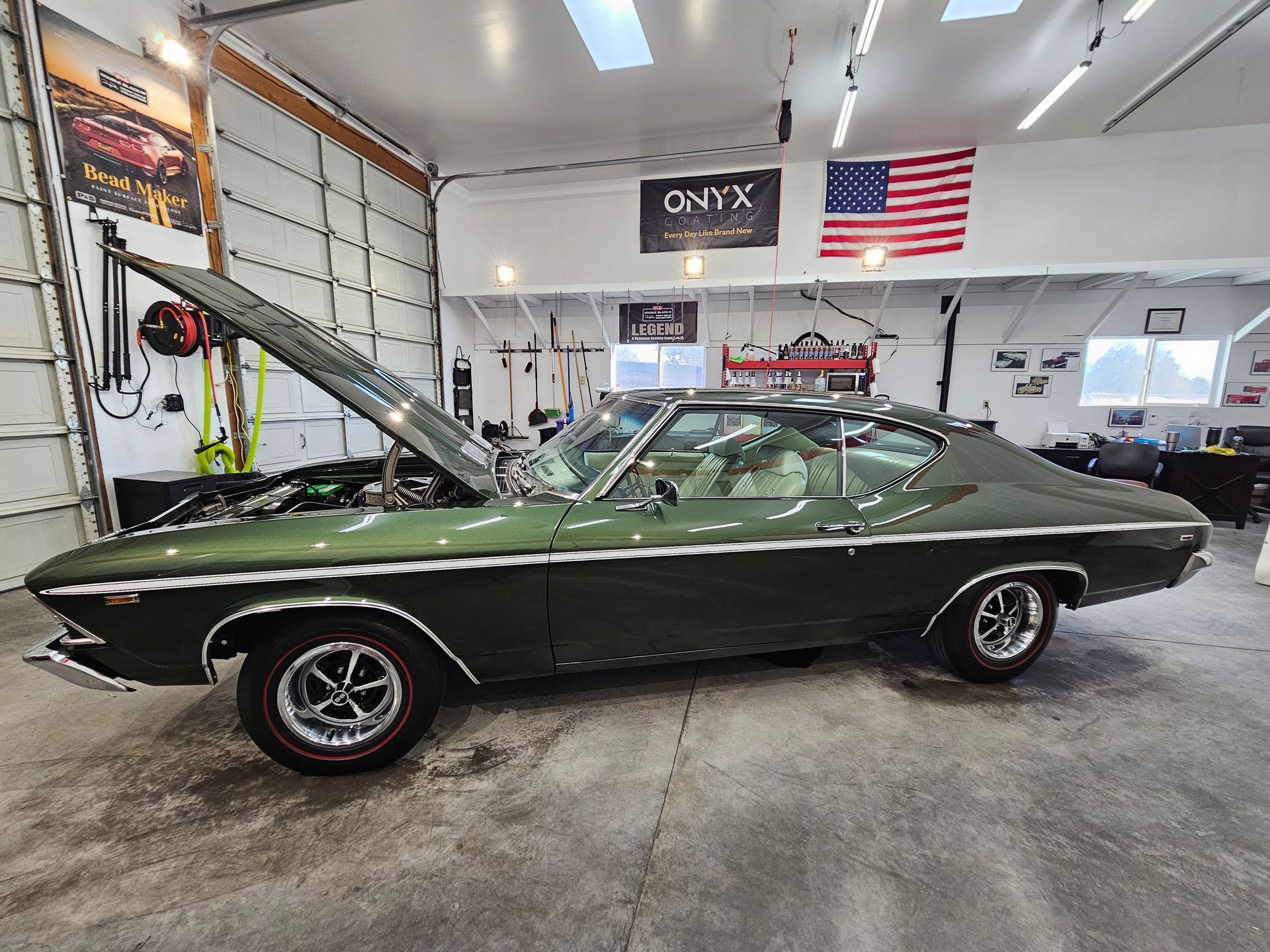 Green classic car with hood up, in a garage with American flag.