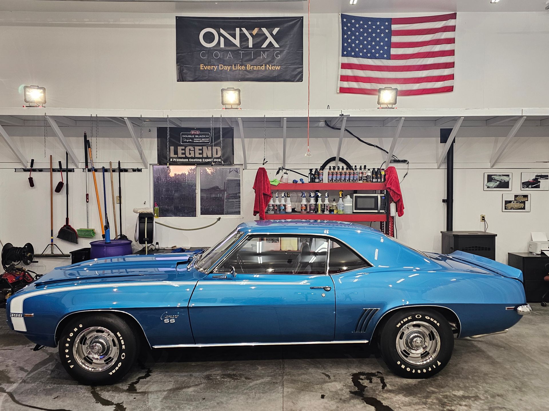 Blue classic Chevrolet Camaro in a garage, with American flag and tools.