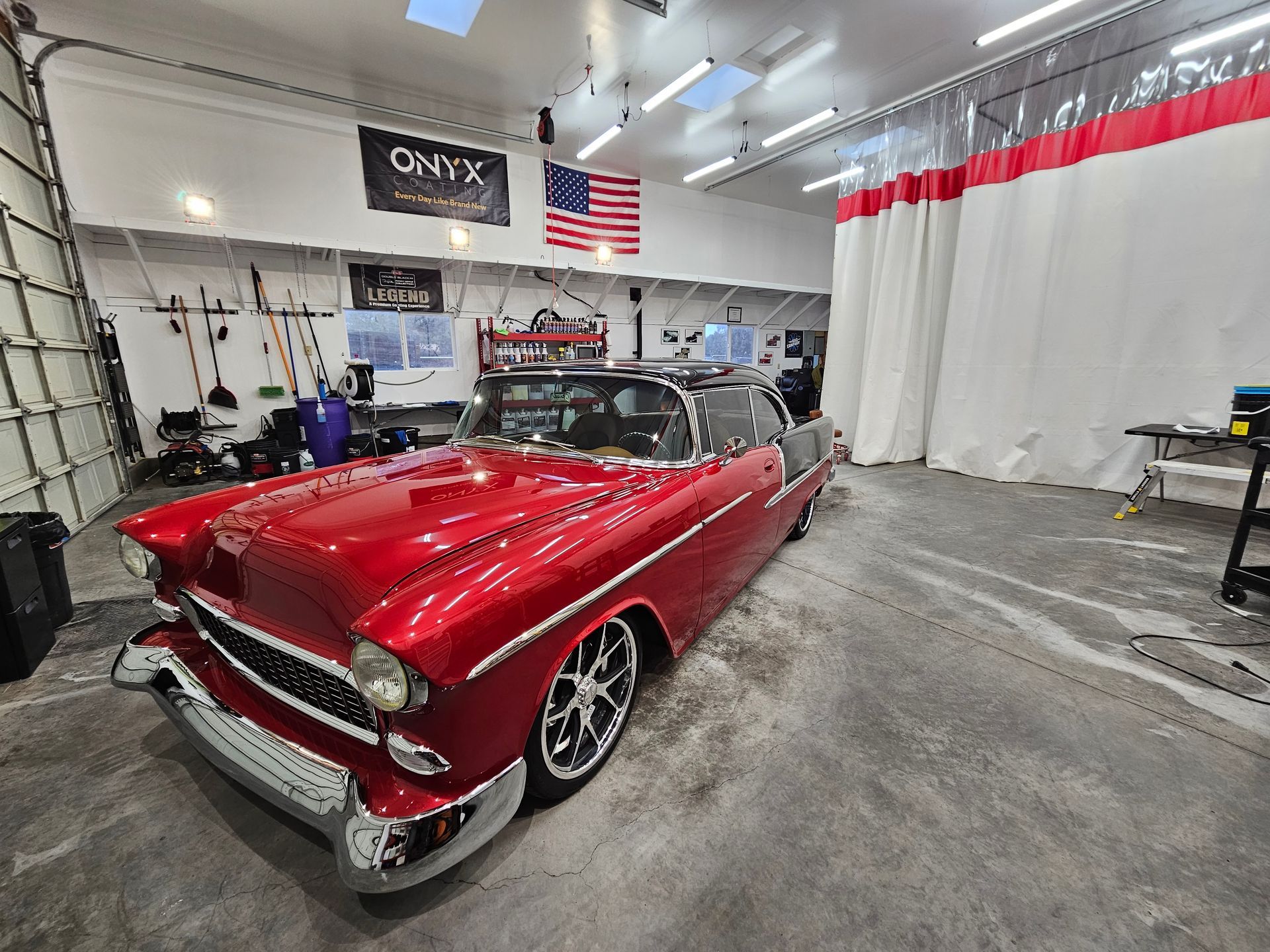 Red classic car in a garage with American flag and cleaning equipment.