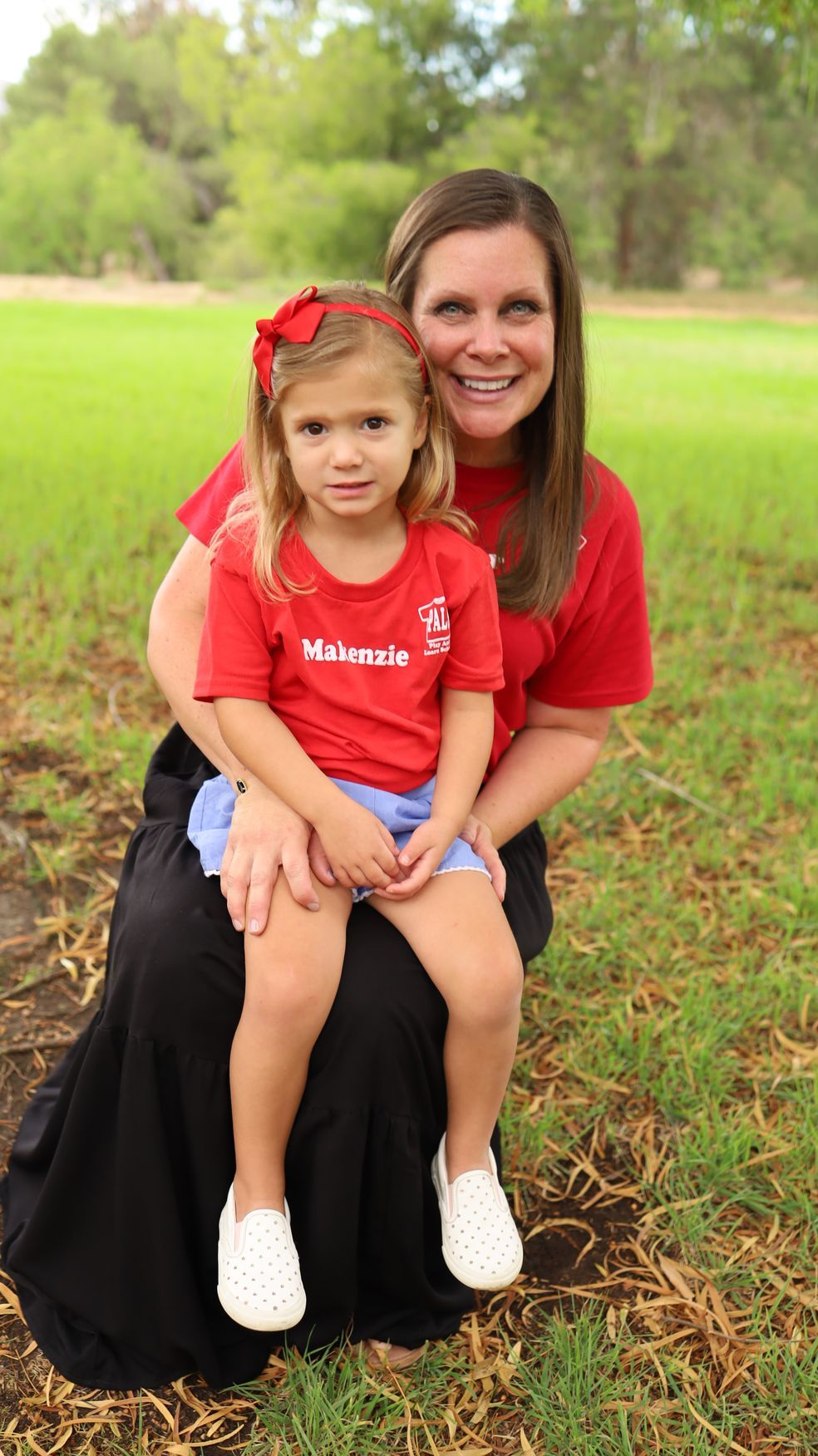 A woman is holding a little girl in her arms in a park.