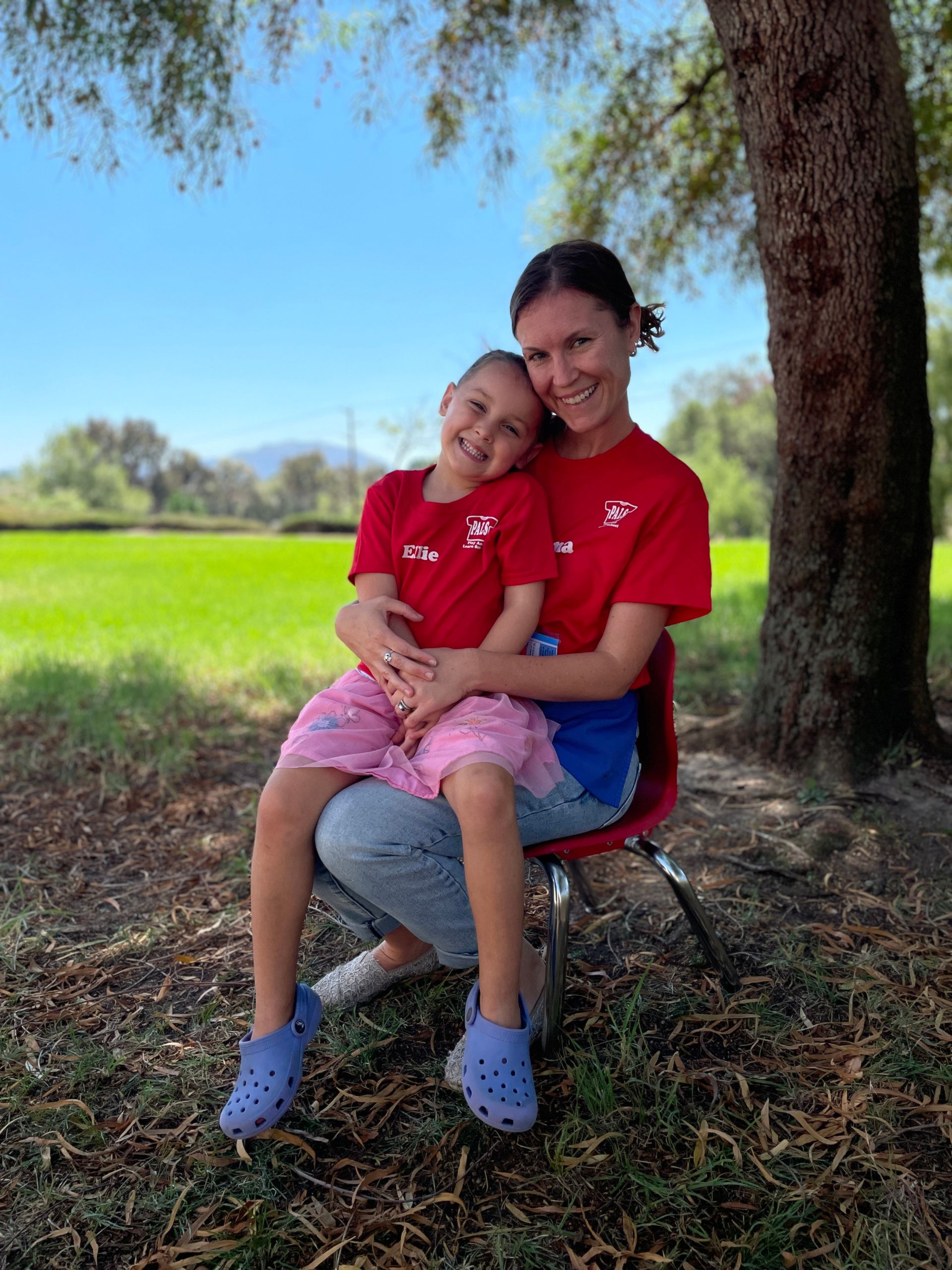A woman is holding a little girl in her arms while standing next to a tree.