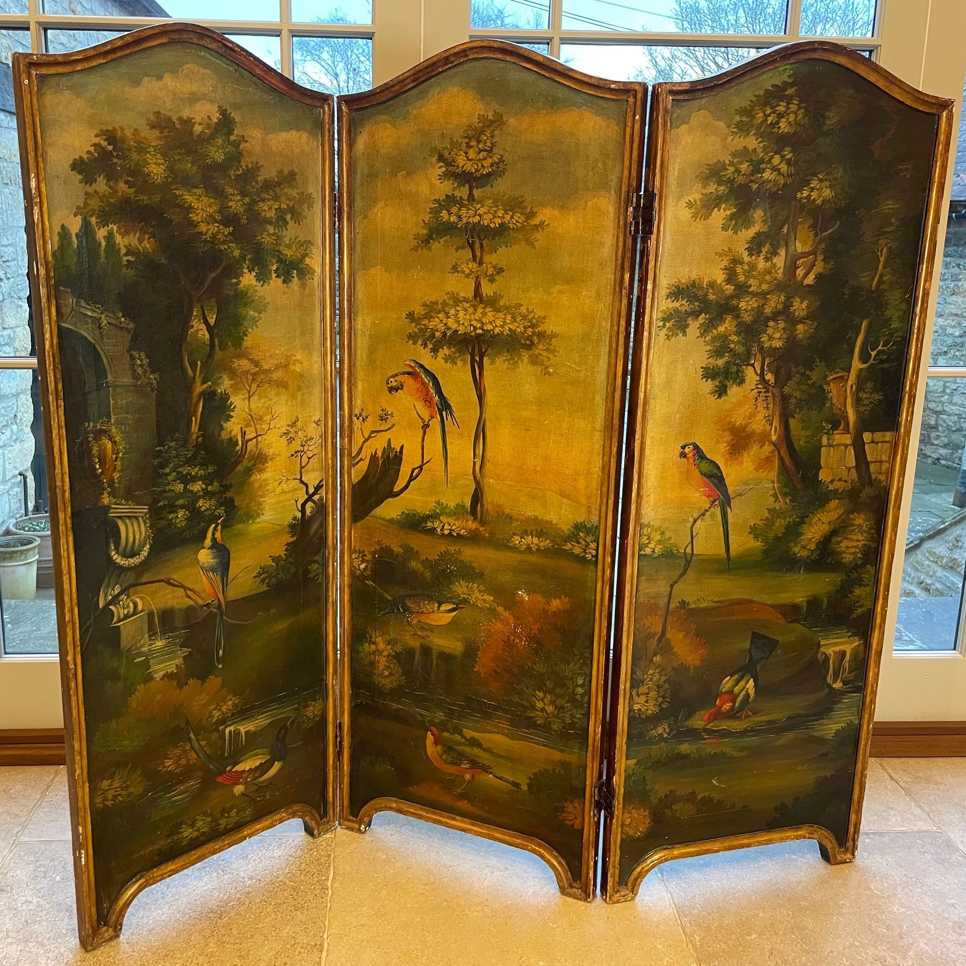 A beautiful screen with 3 panels, depicting parrots and other birds in a clearing surrounded by fantastical woodland and stone architectural features.