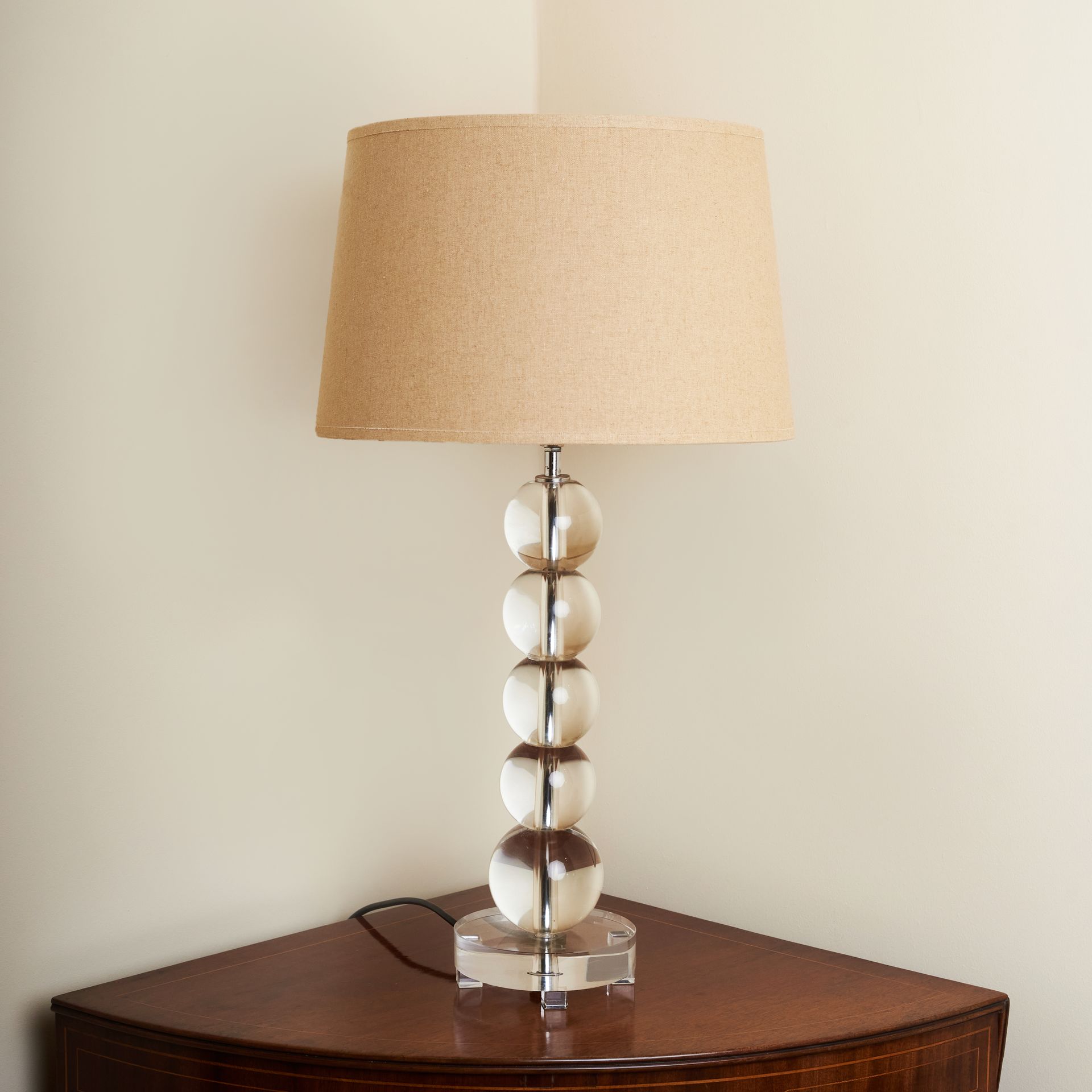 A lamp consisting of a beige lampshade and 5 glass balls stacked on a square glass base.
