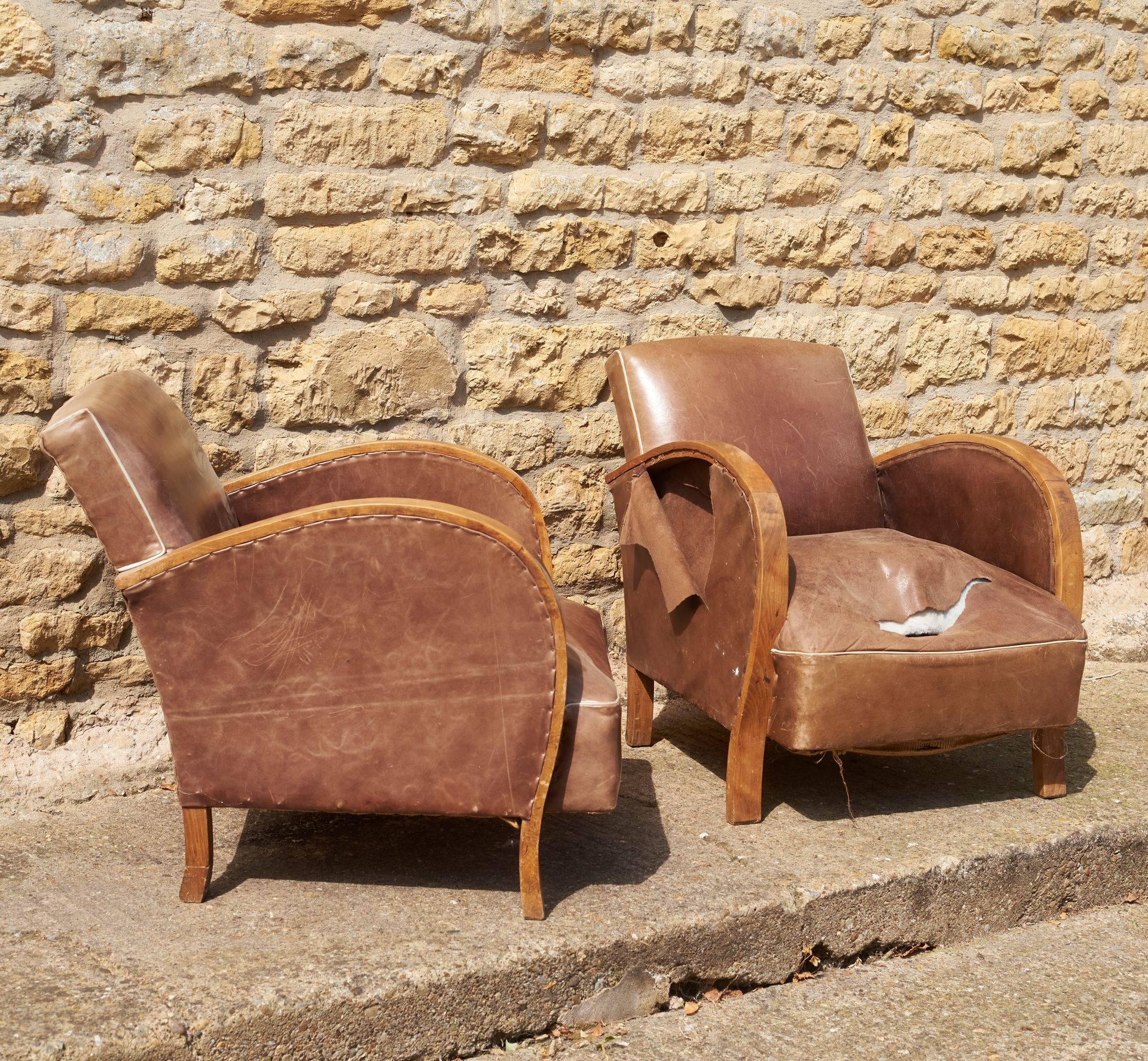 2 leather club chairs with standard rounded arms, one with a rip in the seat.