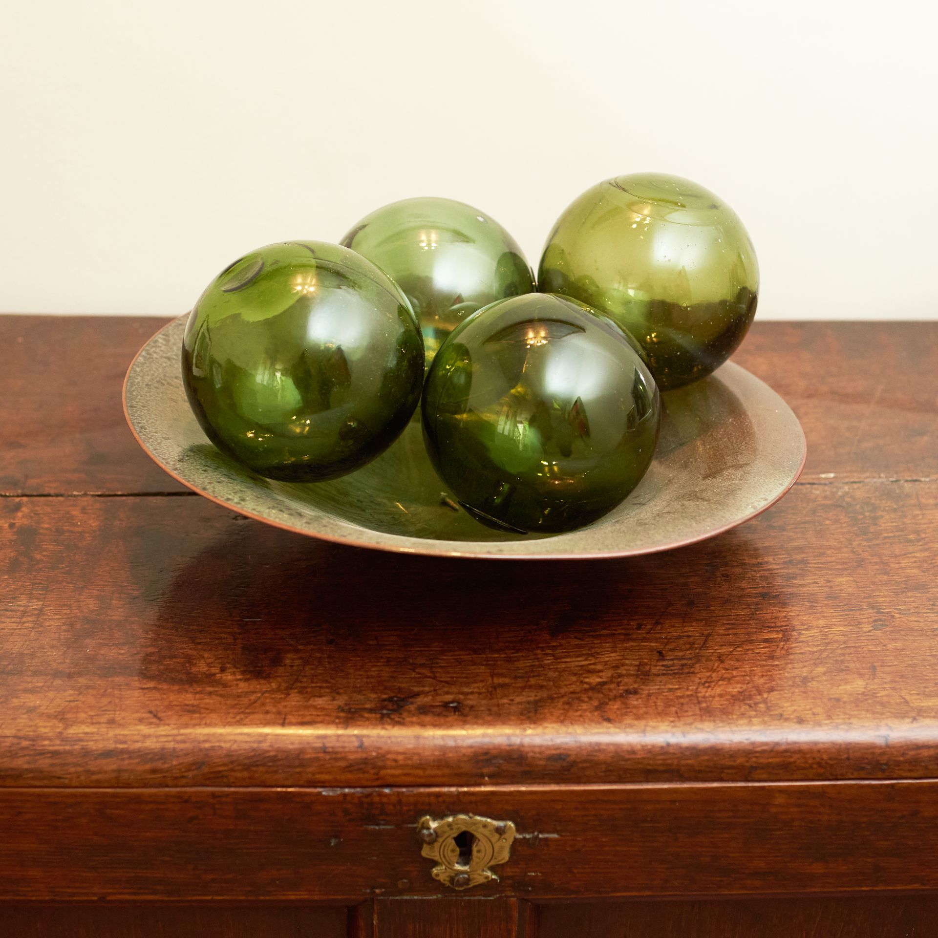 4 handblown glass balls in green, displayed on a brass-metal plate.