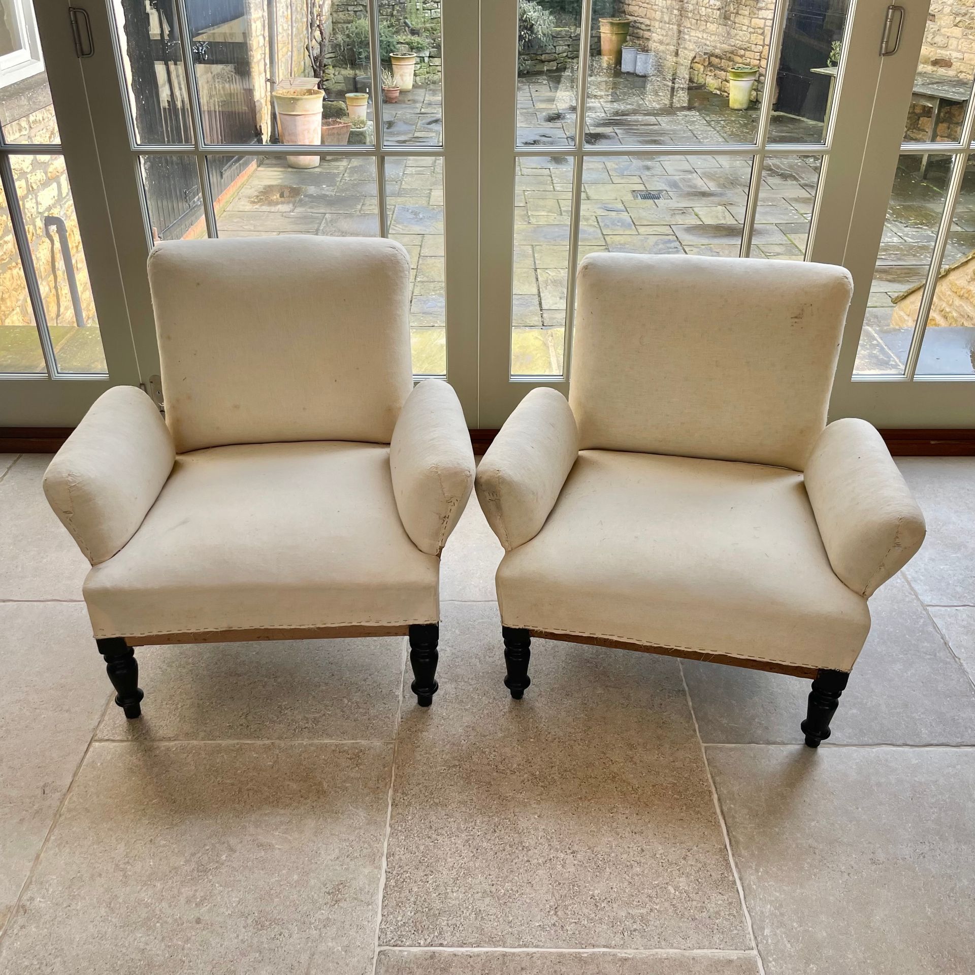 Cream-upholstered 19th century chairs with wooden legs, oblong cushioned arms, and a straight back.