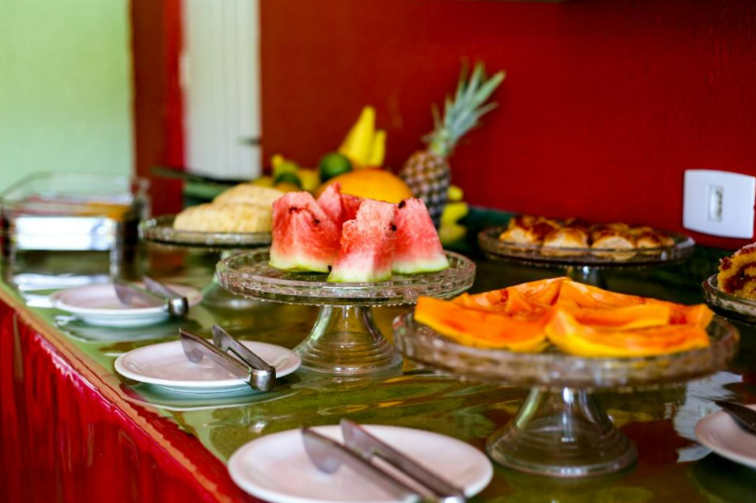 Buffet de café da manhã com melancia fatiada, mamão papaia e doces.