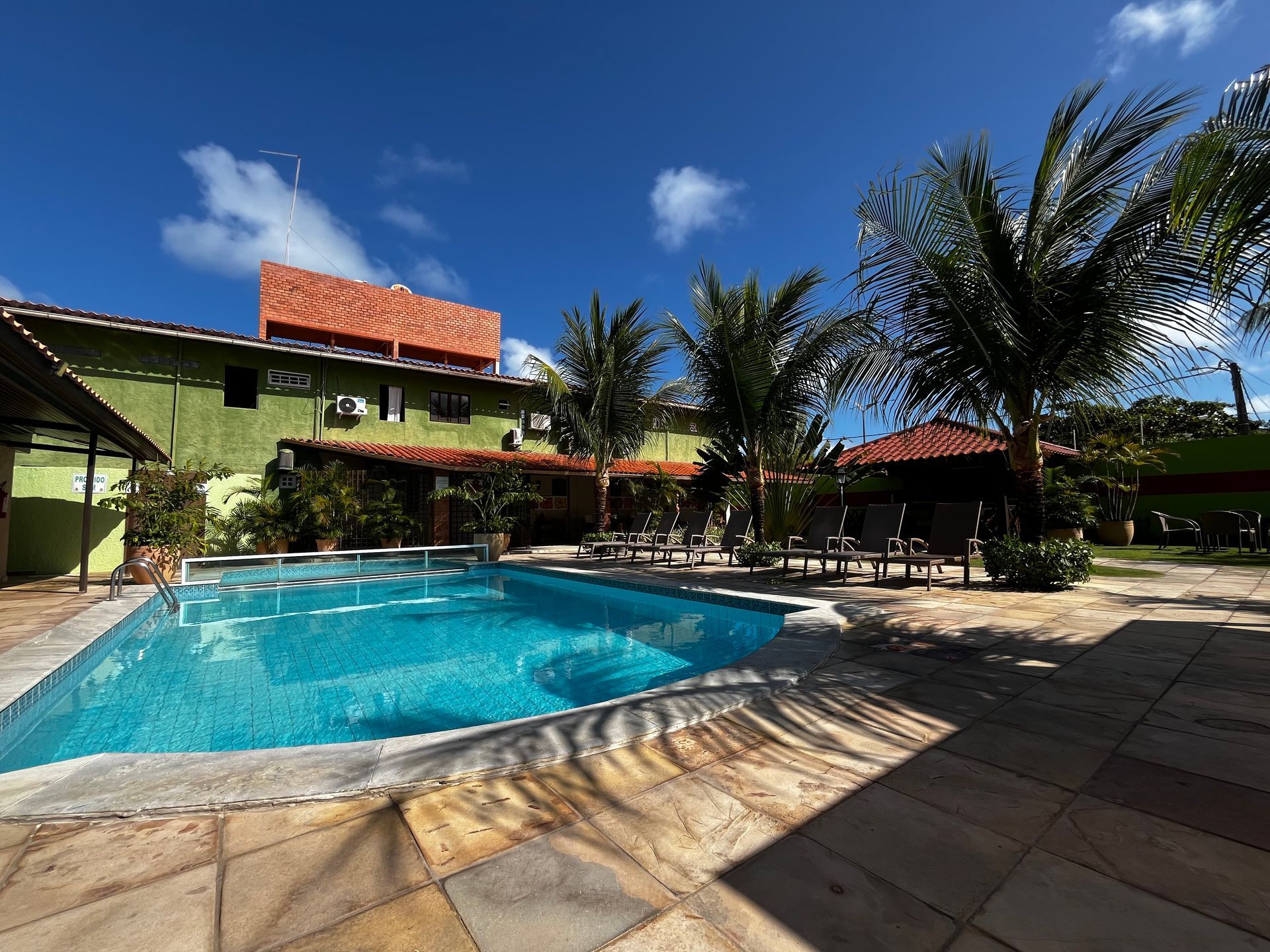 Vista da piscina de um hotel com piscina, palmeiras e céu azul límpido.