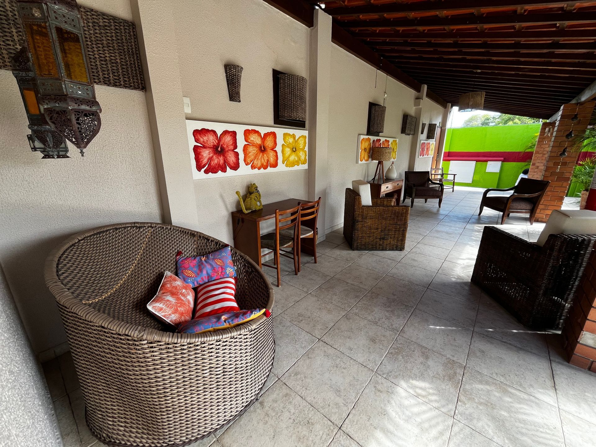 Cadeira de vime com almofadas coloridas, escrivaninha e obras de arte na parede