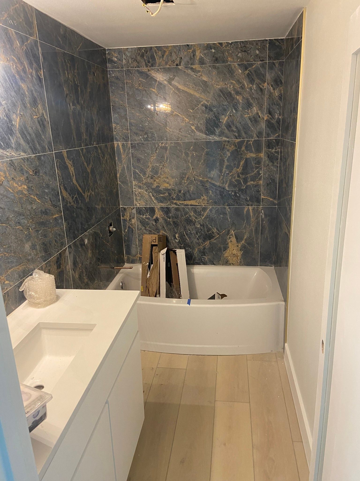 Bathroom with dark blue and gold tiled walls, white vanity, and bathtub under construction.