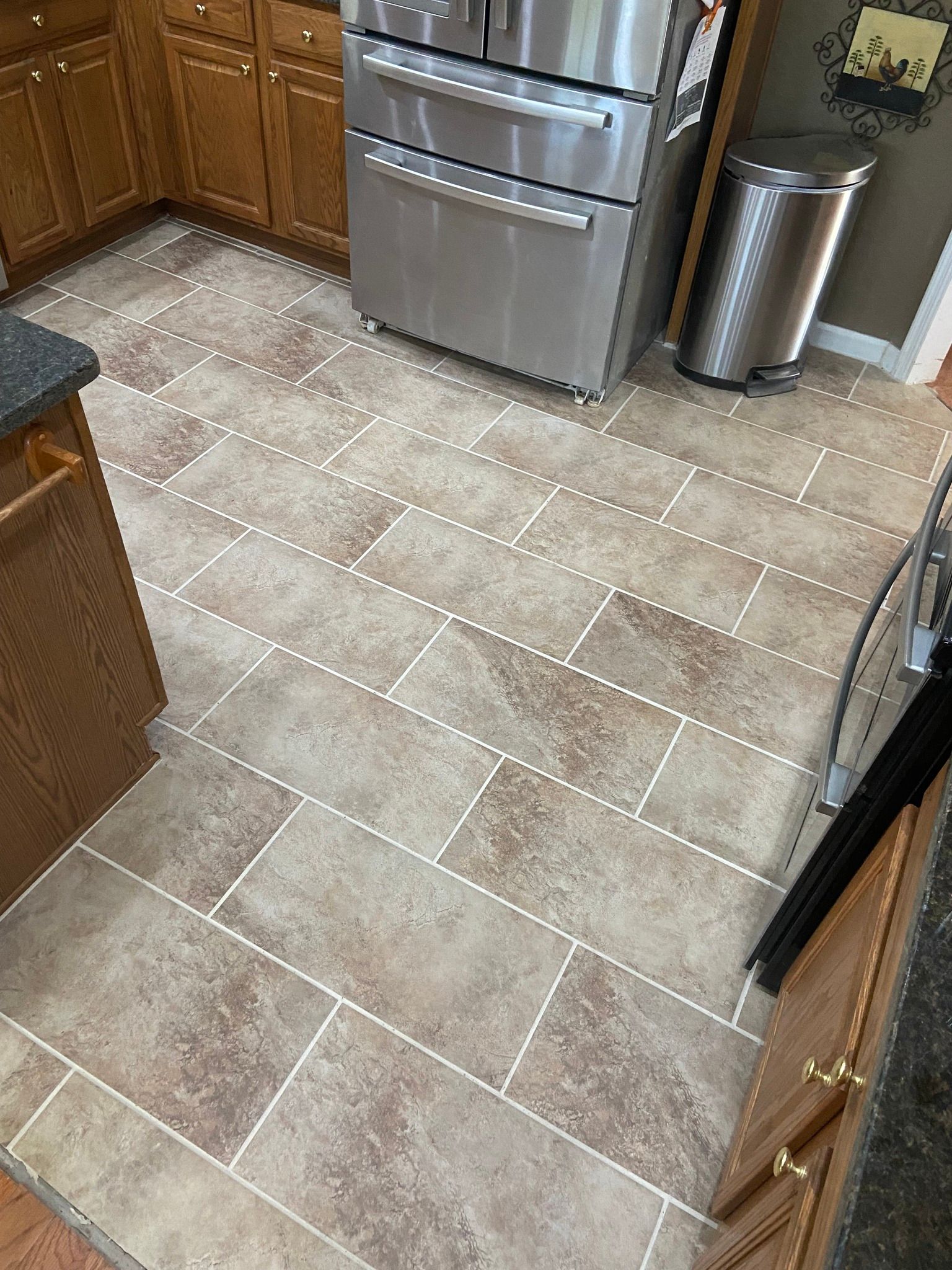 Kitchen with tan rectangular tile flooring, stainless steel appliances, and wooden cabinetry.