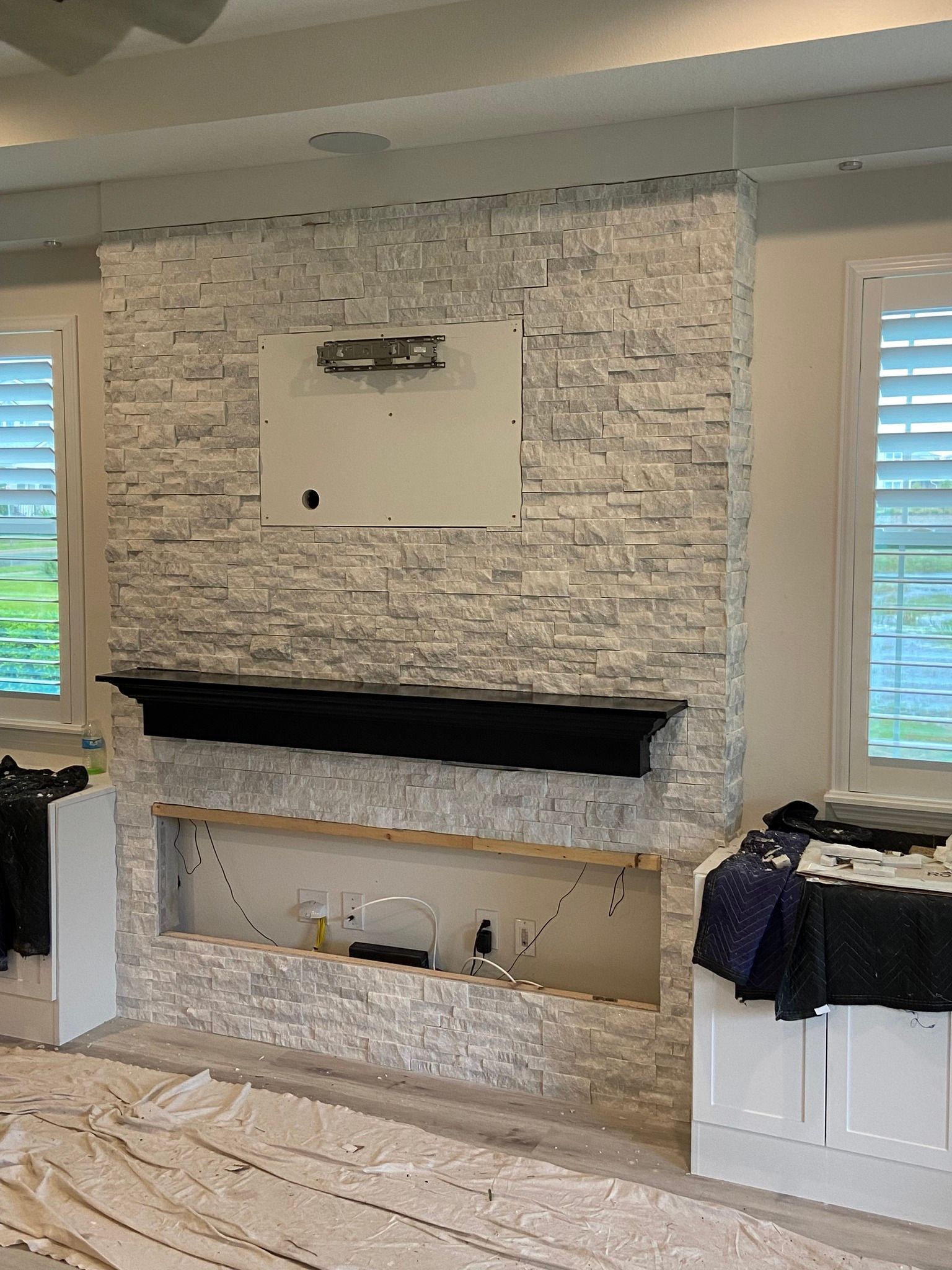 Stone fireplace with black mantel, recessed area, and TV mount; unfinished.