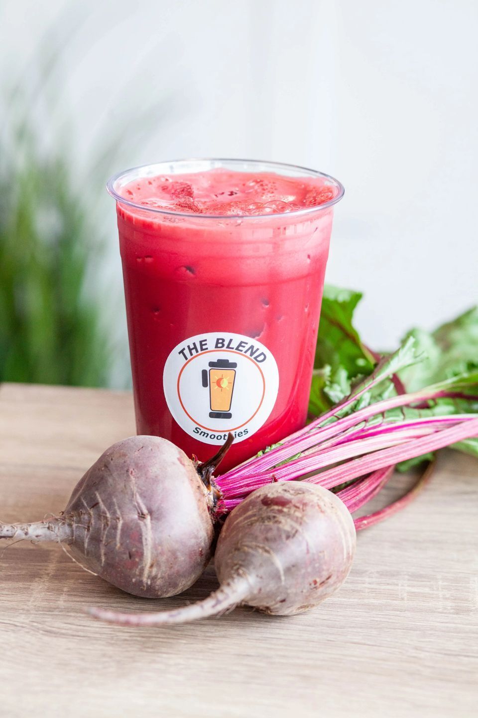 Beet juice in a clear cup with beets and green leaves on a wooden table.