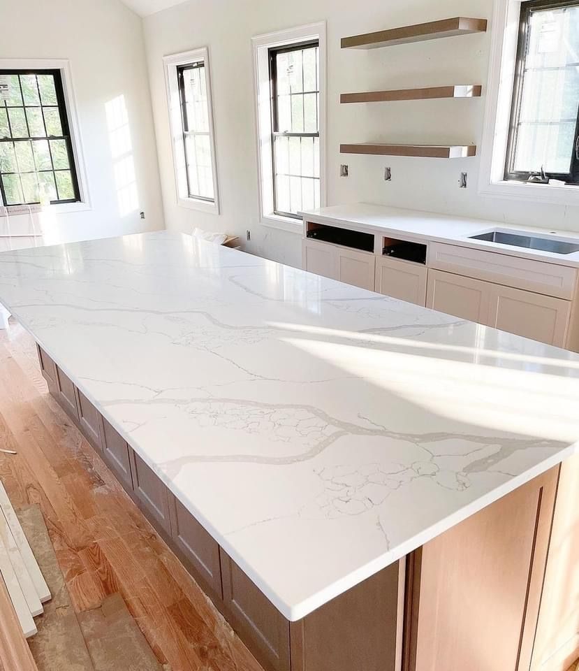 Kitchen island with white quartz countertop and gray cabinets under windows.