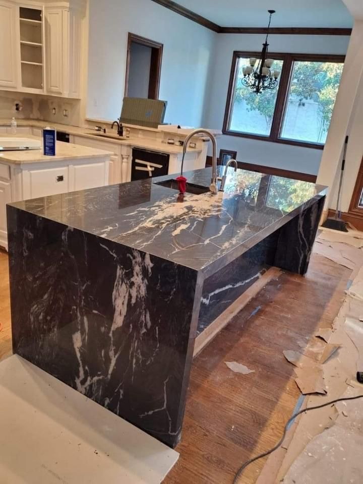 Kitchen island with dark granite countertop and integrated sink; wood floor, unfinished walls.
