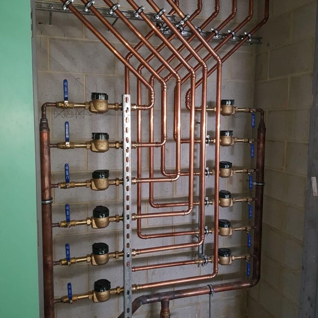 Copper pipes connected to brass valves and meters on a concrete block wall.