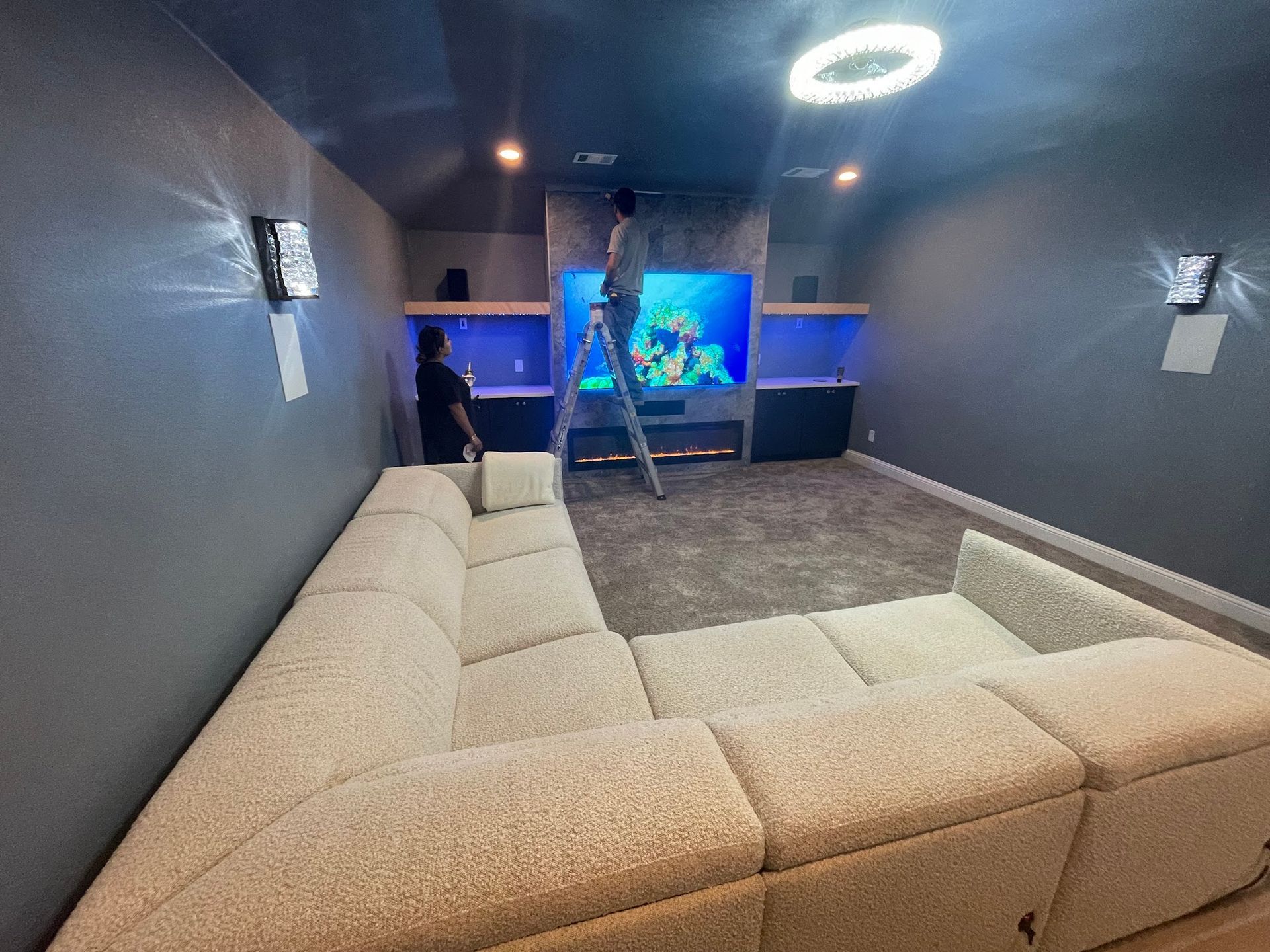 A home theater with a large sectional sofa, TV, and two people working.