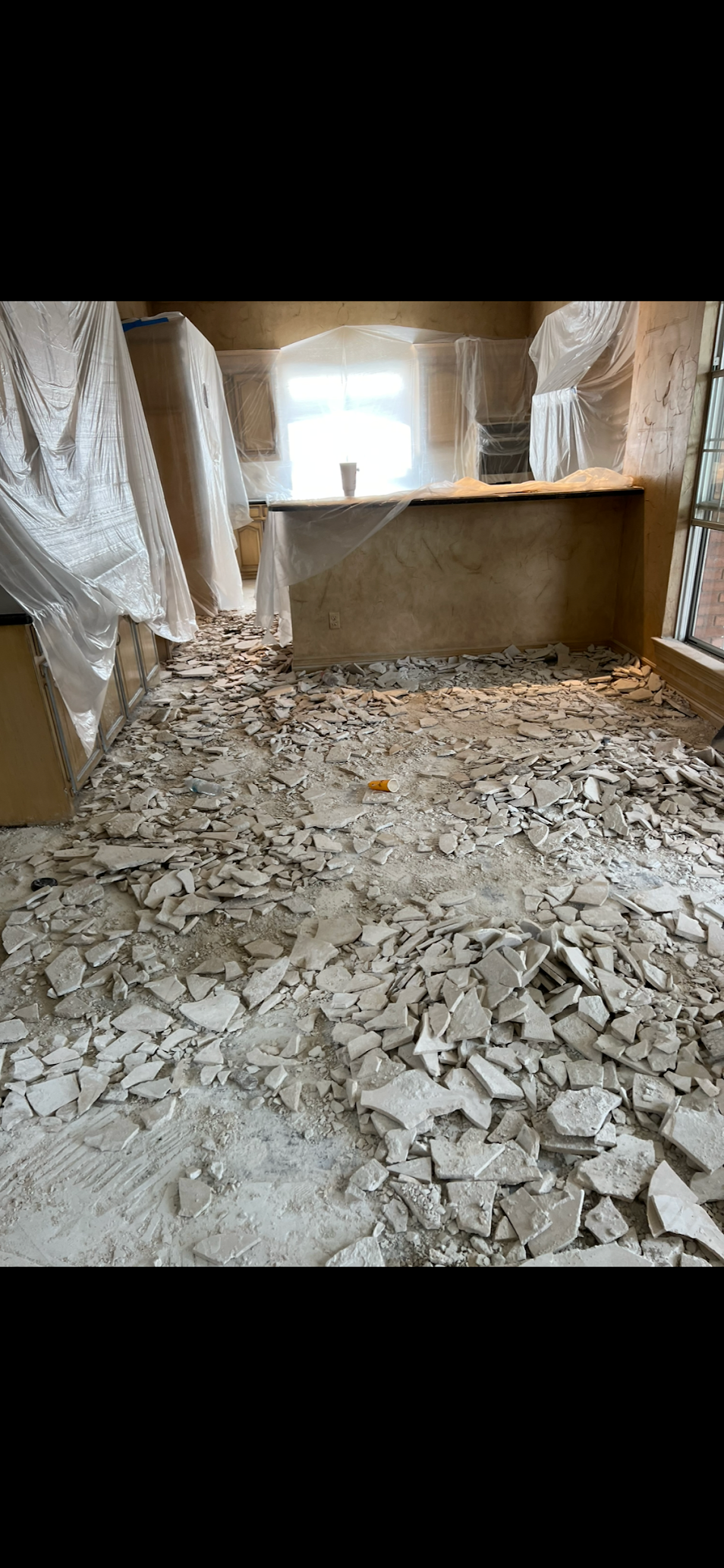 A room under construction; debris covers the floor, with a covered counter and window in the background.