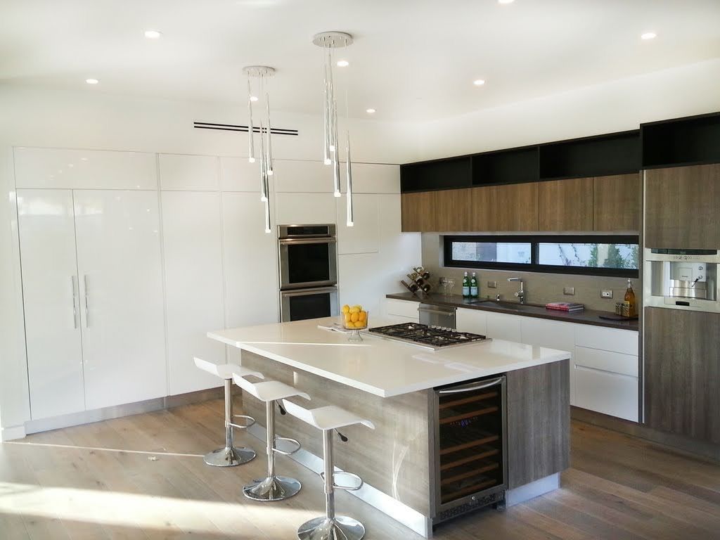 Modern kitchen with white island, stainless steel stools, and built-in appliances. Wooden cabinets and flooring.