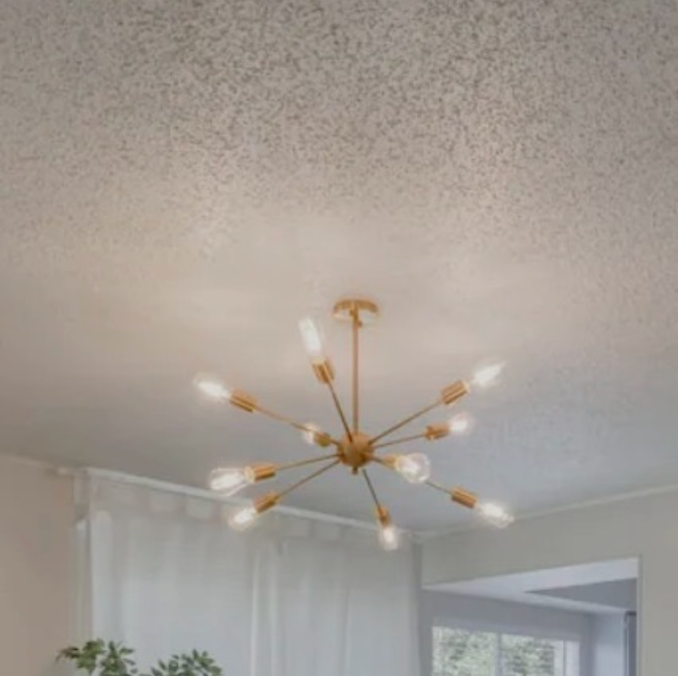 Gold starburst chandelier hanging from a textured white ceiling, near a window.