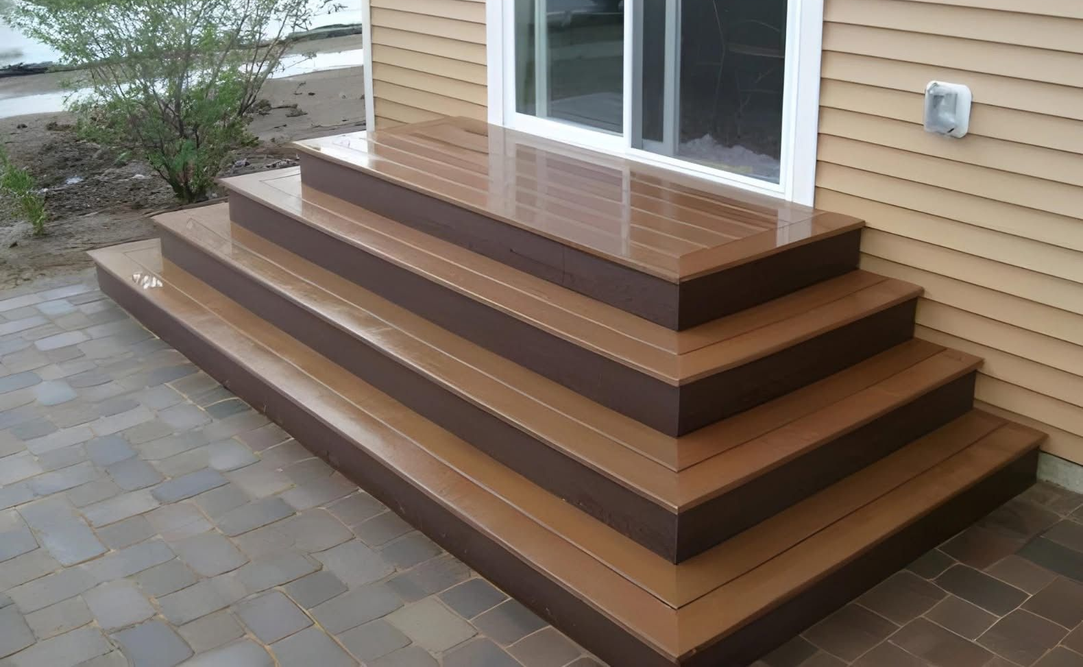 Woman in green gloves and jacket spraying plants in a greenhouse, smiling.