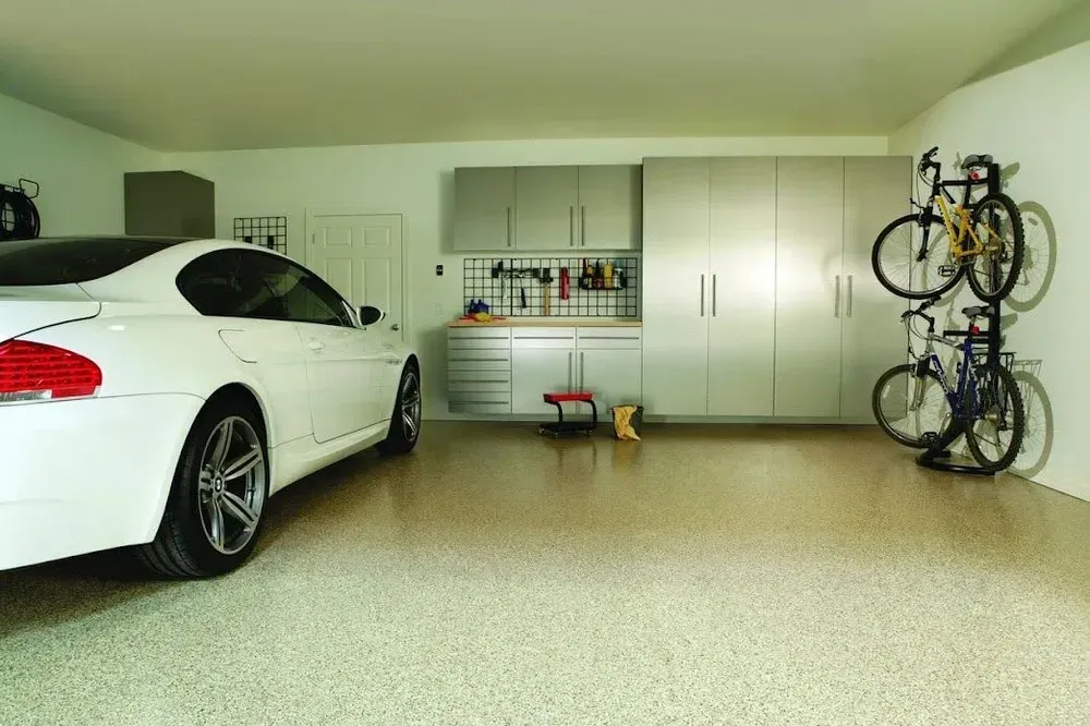 White car in a clean, modern garage with storage cabinets, a workbench, and bicycles on the wall.