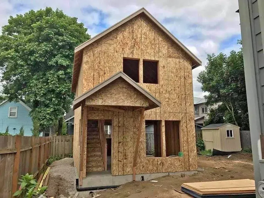 Two-story house under construction, with exposed wood frame and small porch.
