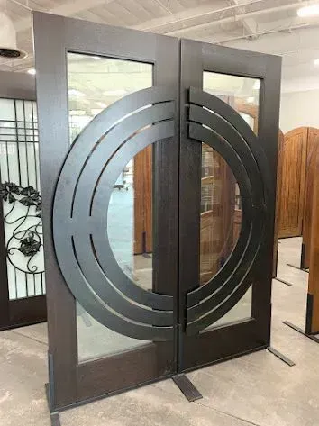 Woman in gloves and apron sprays plants, smiling in a greenhouse setting.