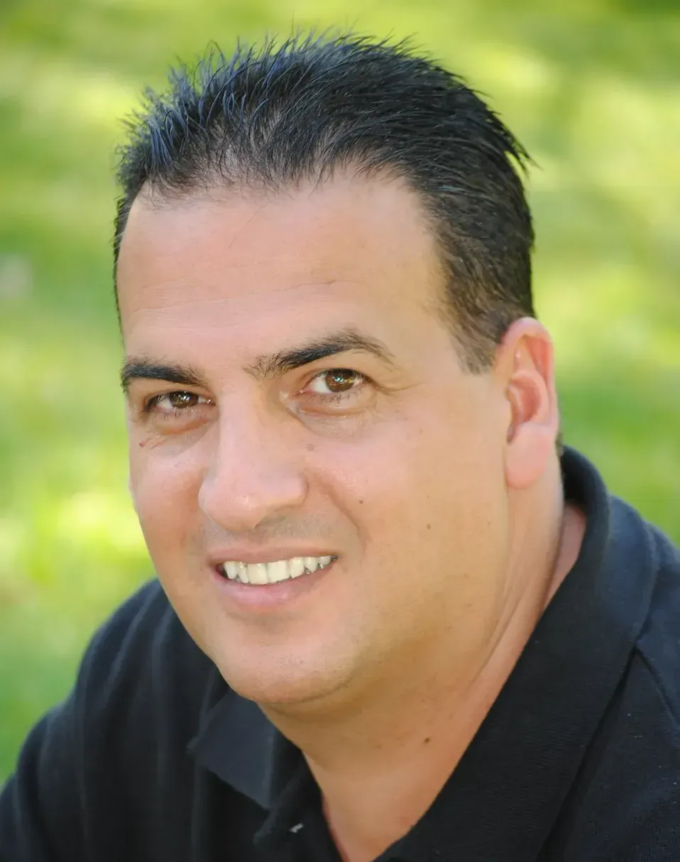 Man with dark hair and a black shirt smiling outdoors.