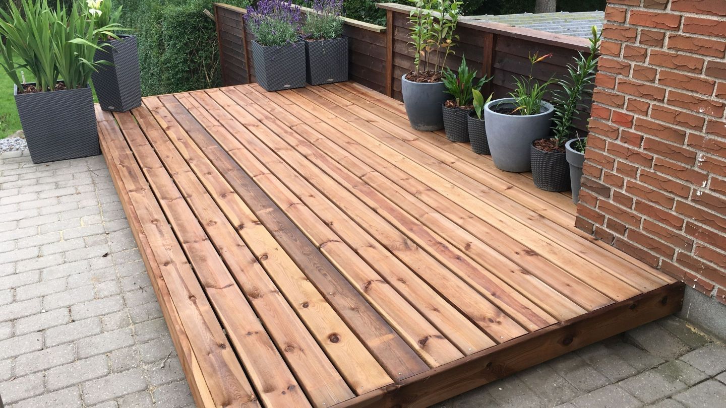 A wooden deck with potted plants on it next to a brick wall.