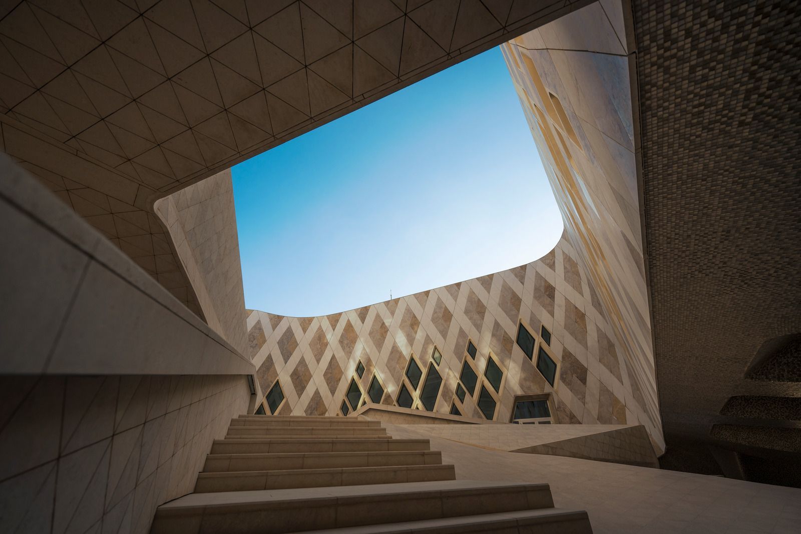 Stone stairs leading up to an open-air building with diamond-patterned walls against a blue sky.