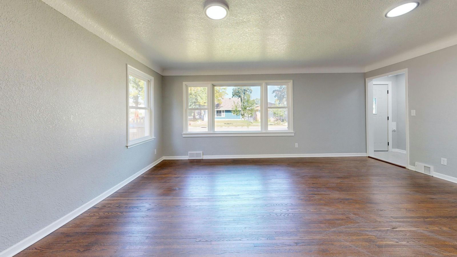 Empty room with hardwood floors, light gray walls, and several windows.