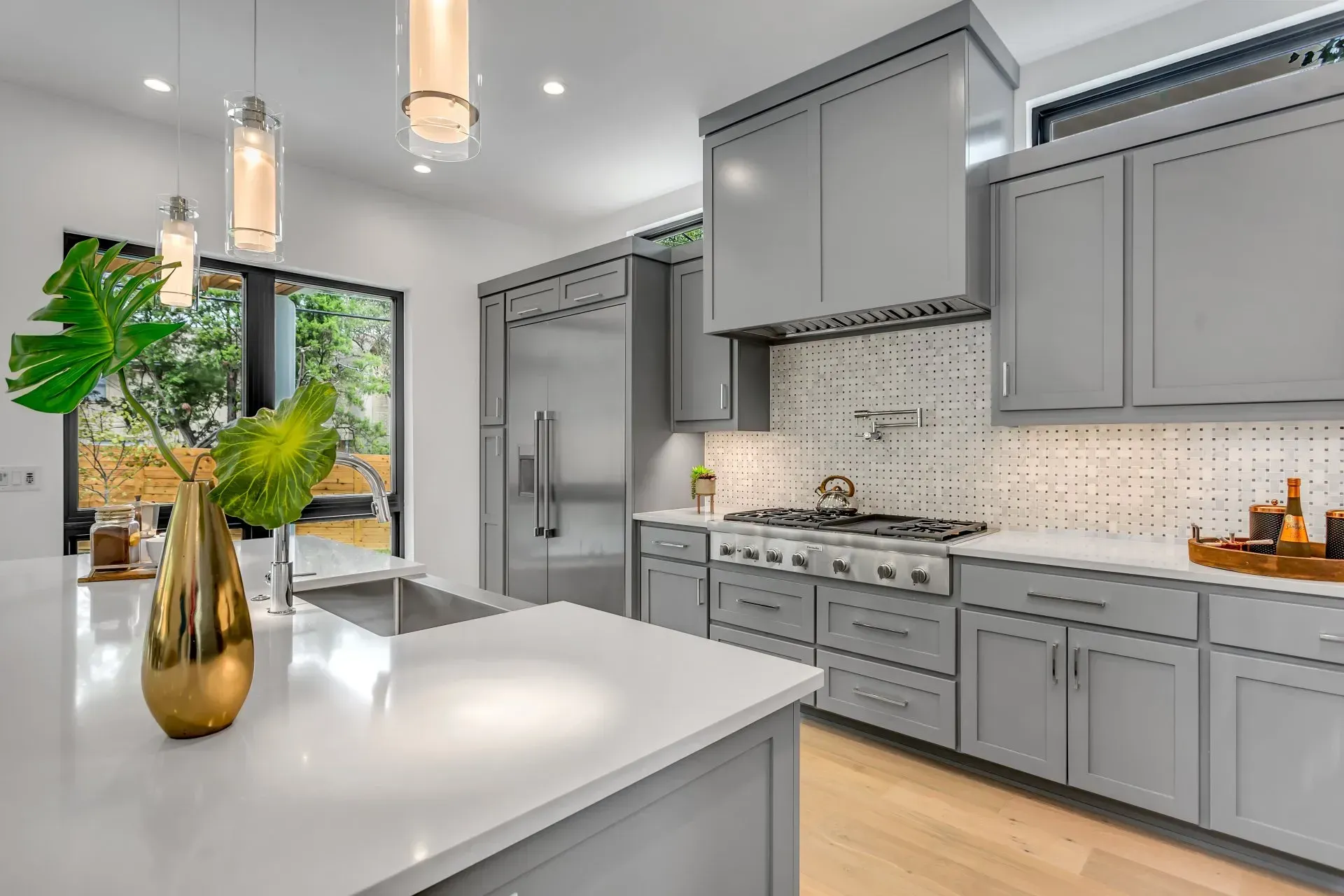 Modern gray kitchen with white countertops, stainless steel appliances, and island with a gold vase.