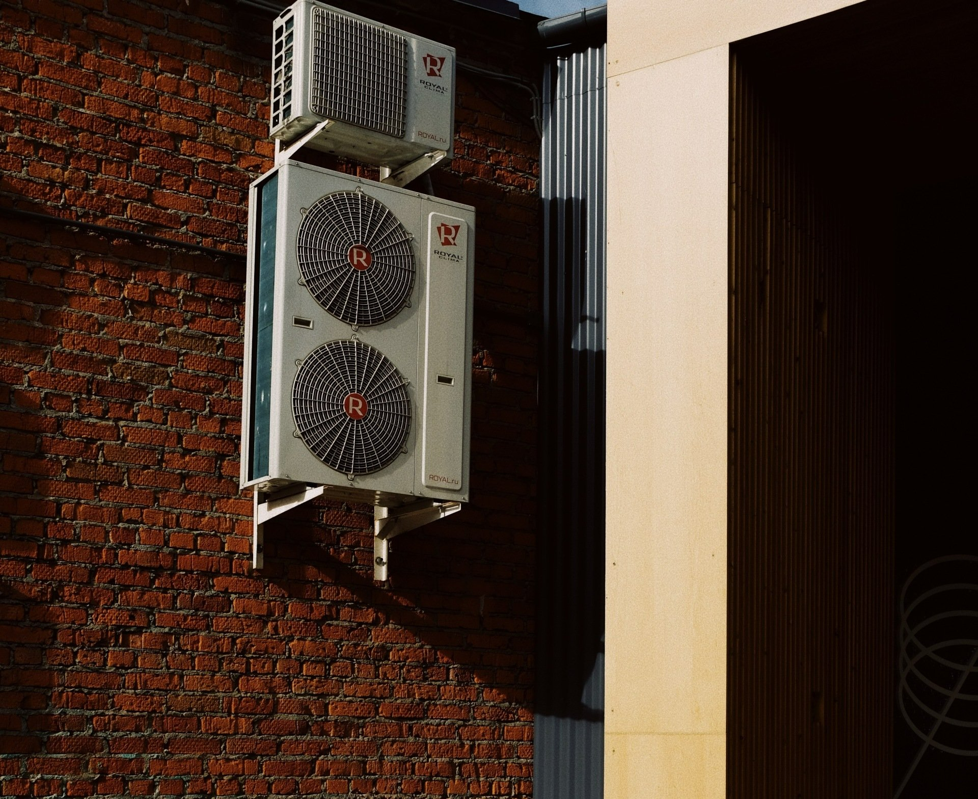 A large air conditioner is mounted to the side of a brick building