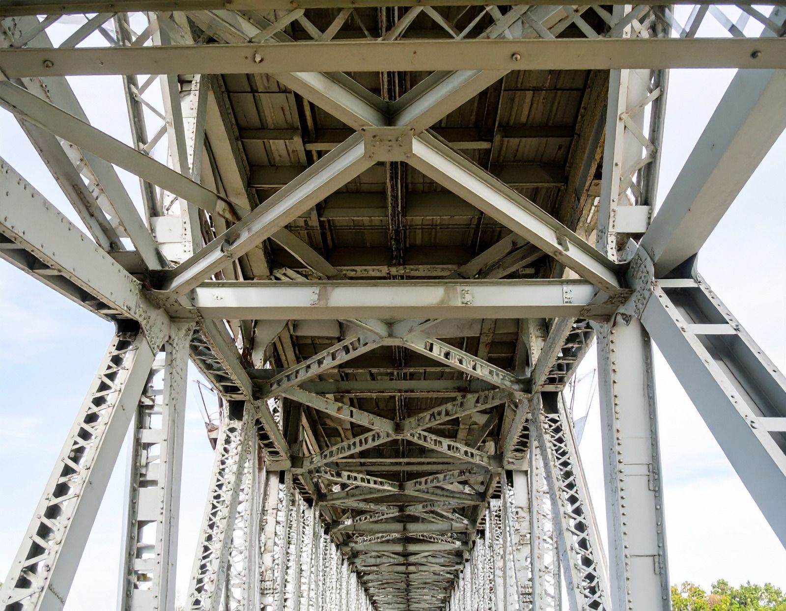 Steel bridge structure, underside view, crisscrossing beams, wooden deck.