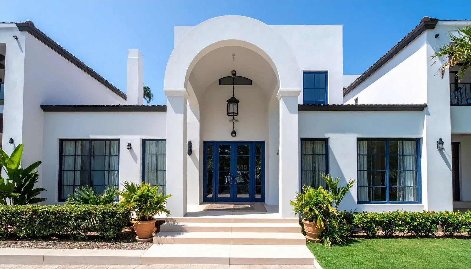 White stucco home with a blue front door, archway, and black-framed windows.