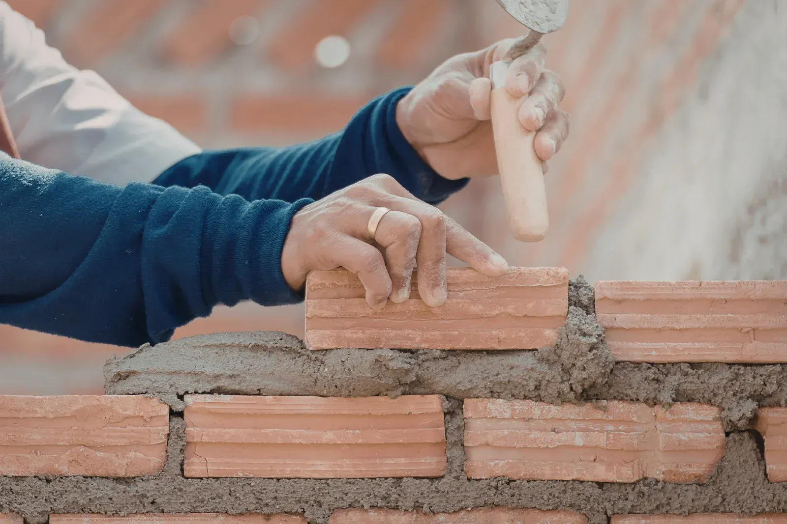 Woman in green overalls and gloves spraying plants in a greenhouse, smiling at the camera.