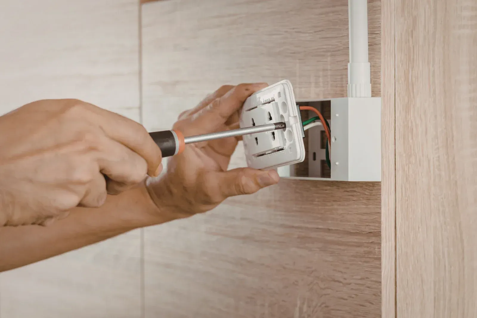 Person installing a white electrical outlet on a wood-paneled wall with a screwdriver.